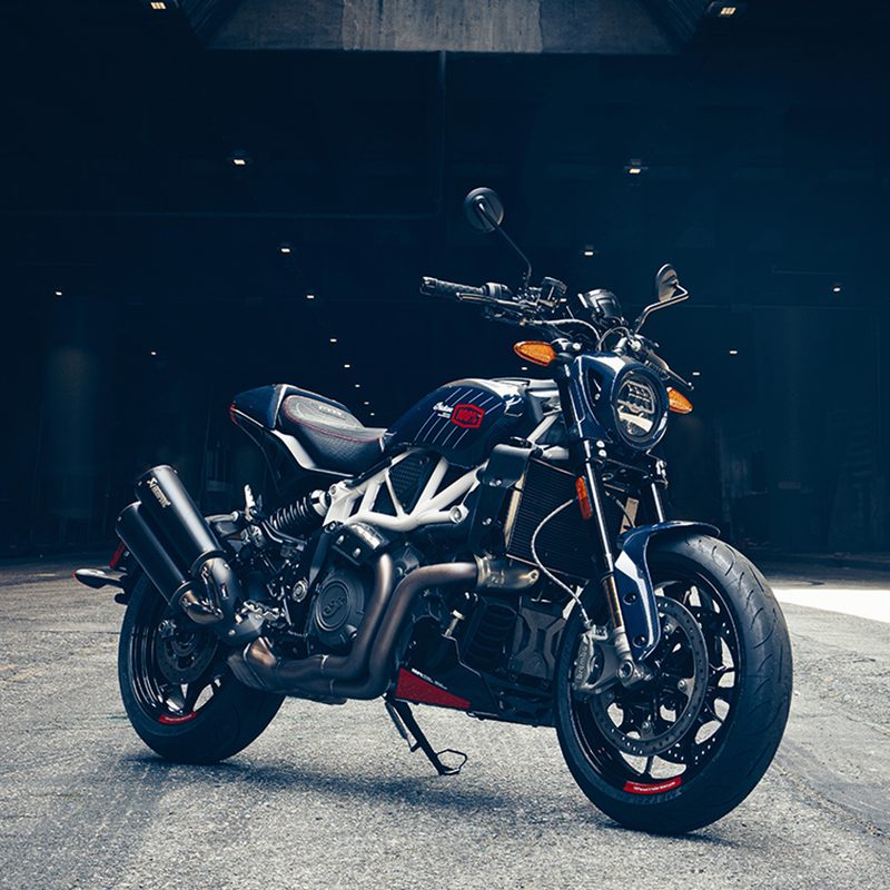 Left front three-quarter view of an Indian Motorcycle 2024 FTR x 100% R limited edition on a light gray floor with a dark background with pin lights