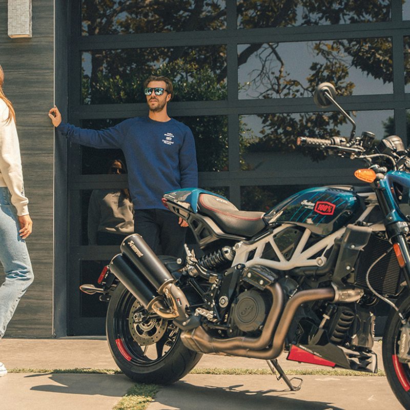 Two people facing each other talking to the left of an Indian Motorcycle 2024 FTR x 100% R limited edition