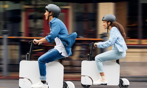 Two people riding Honda Motocompacto escooters on a city street.