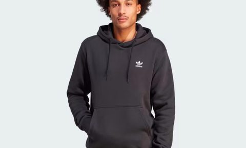 A model wears a black Adidas Trefoil Essentials Hoodie against a gray background.