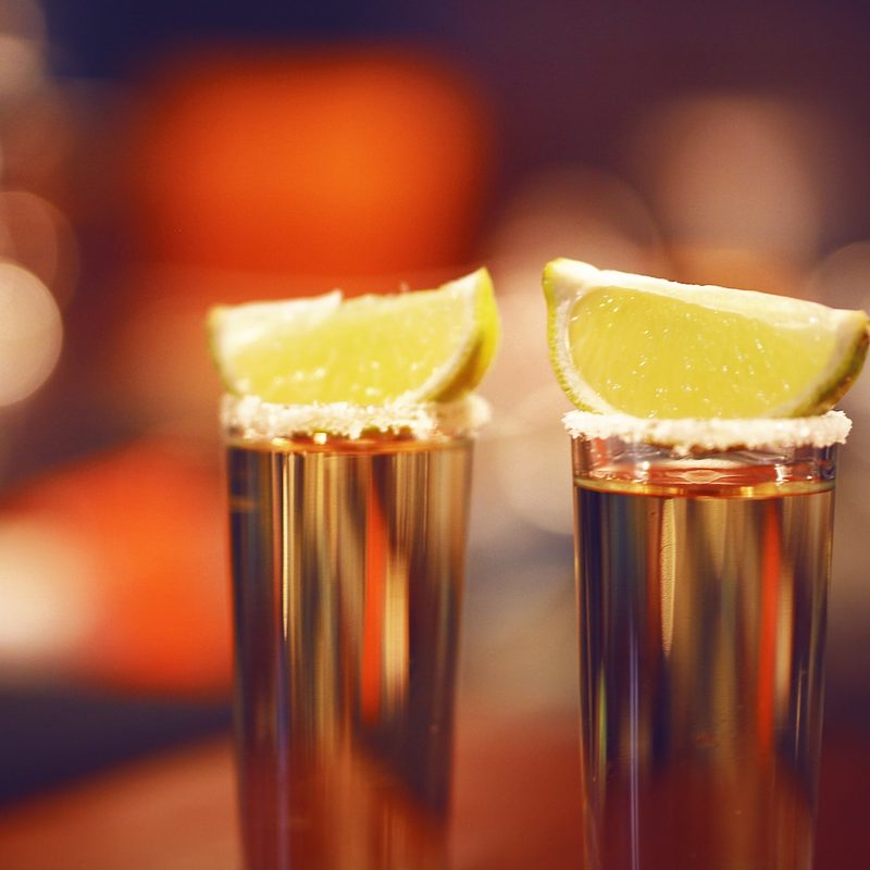 Two shots of tequila in shot glasses with lemons on top