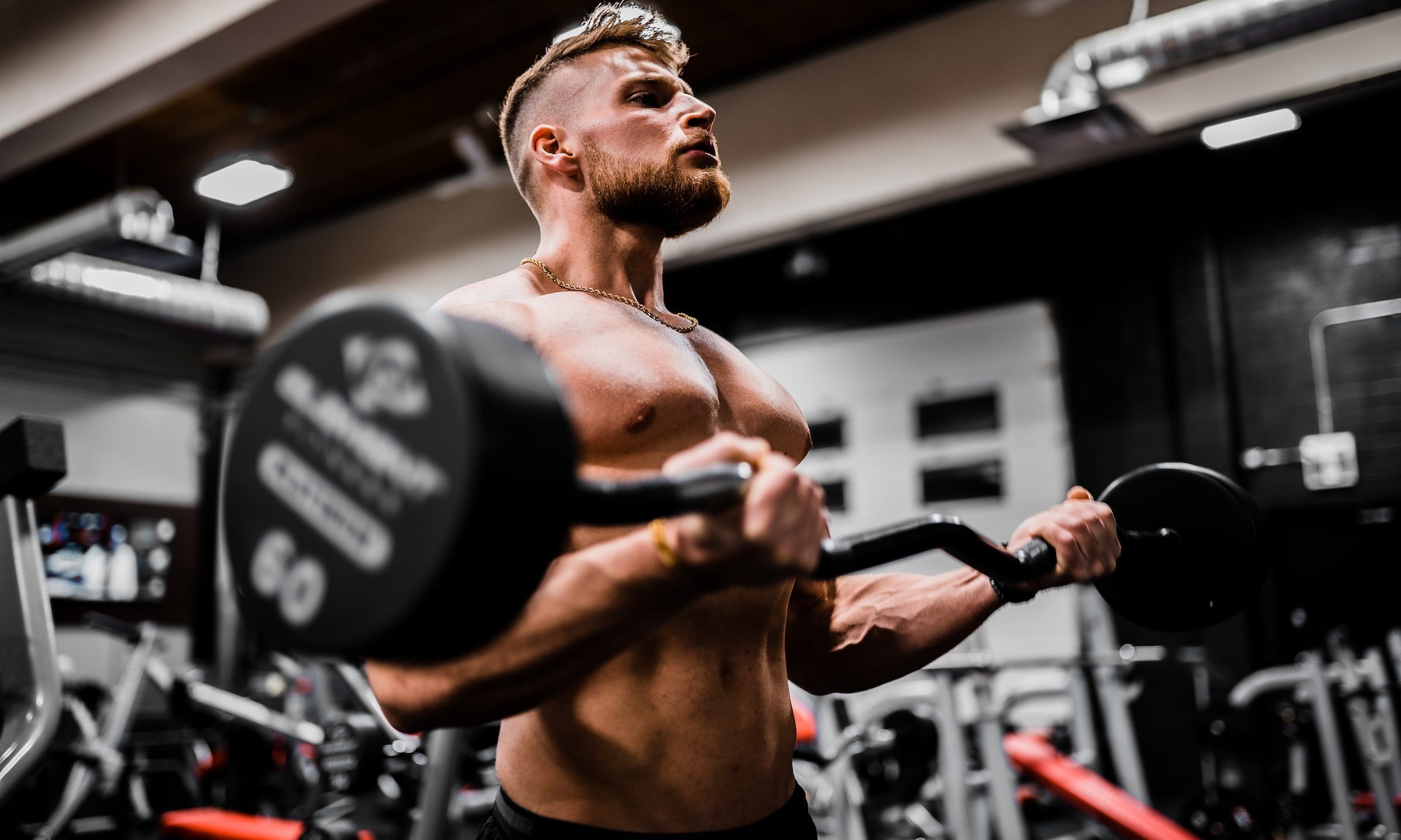 Man working out lifting weights strength training shirtless in gym