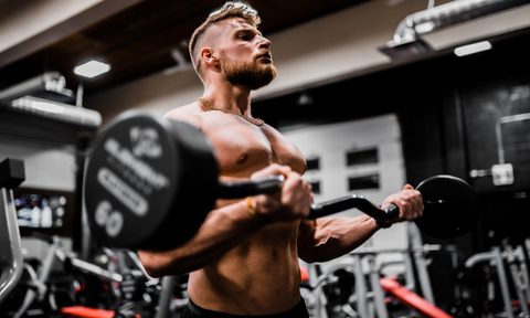 Man working out lifting weights strength training shirtless in gym