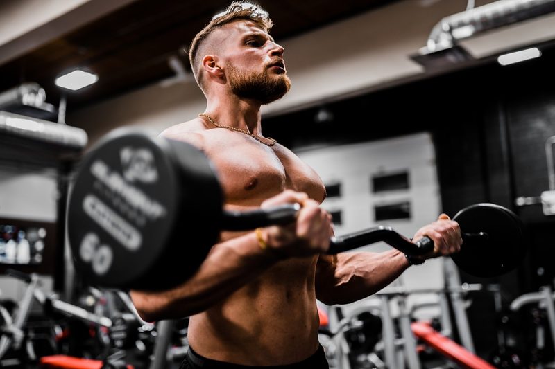 Man working out lifting weights strength training shirtless in gym