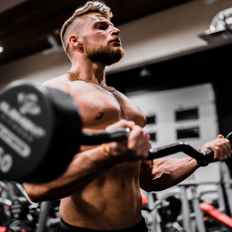 Man working out lifting weights strength training shirtless in gym