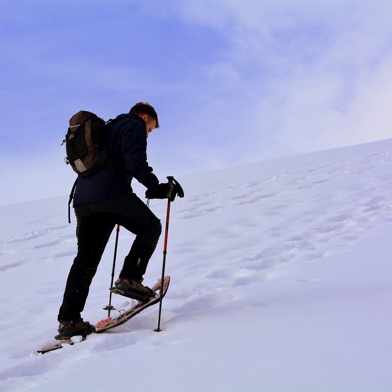 Male hiker walking up a snowy hill in snow shoes and trekking poles