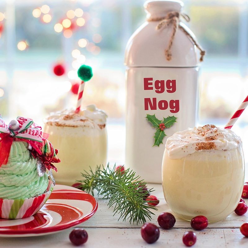 Glass and container of egg nog with cupcake on table