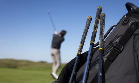 Man hitting a golf ball behind a bag of clubs.