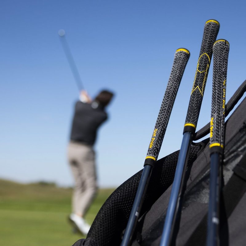 Man hitting a golf ball behind a bag of clubs