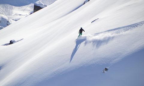 A man snowboarding across an open mountainside ready to drop-in.