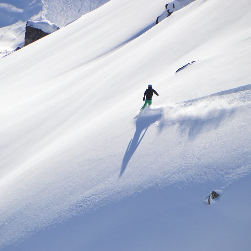 A man snowboarding across an open mountainside ready to drop-in.