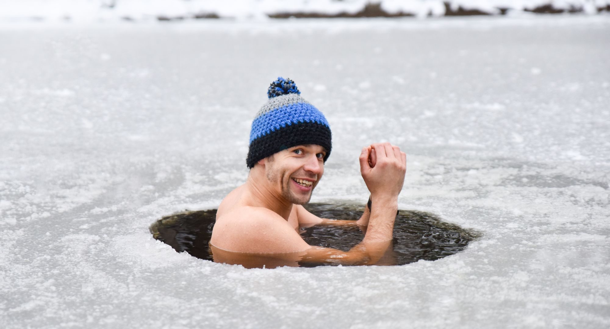 Man in ice water smiling with a beanie on his head
