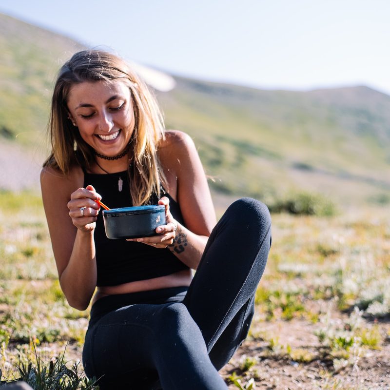 Young woman sitting outside enjoying a meal bowl mug