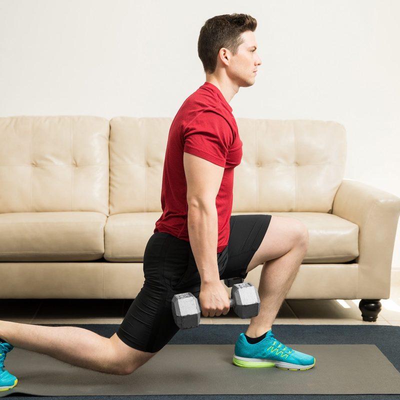 Profile view of a man lunge red shirt young and fit man doing kneeling lunges with a pair of dumbbells at home