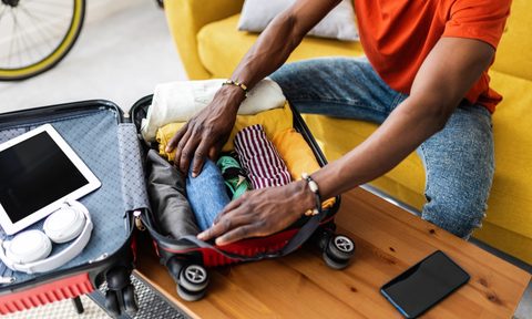 Close up hands of young african man packing luggage before going on vacation. Travel and vacation concept.
