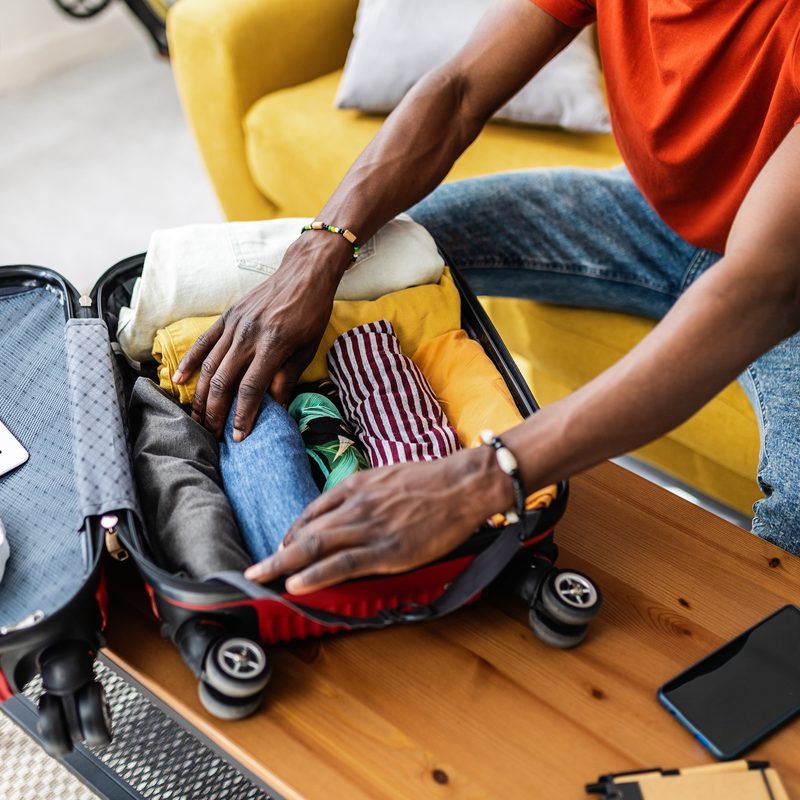 Close up hands of young african man packing luggage before going on vacation. Travel and vacation concept.
