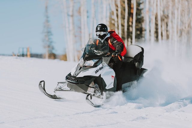 A guy on a snomobile driving through the snow in the woods