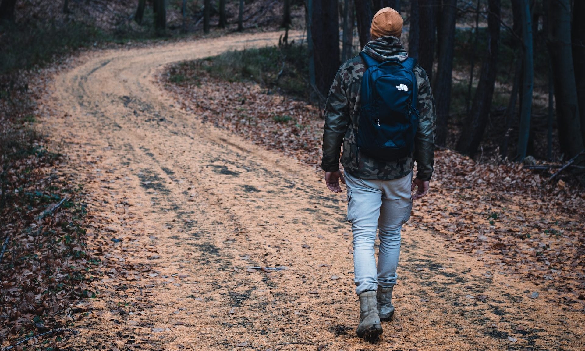 man wearing hat walking through winding hiking trail