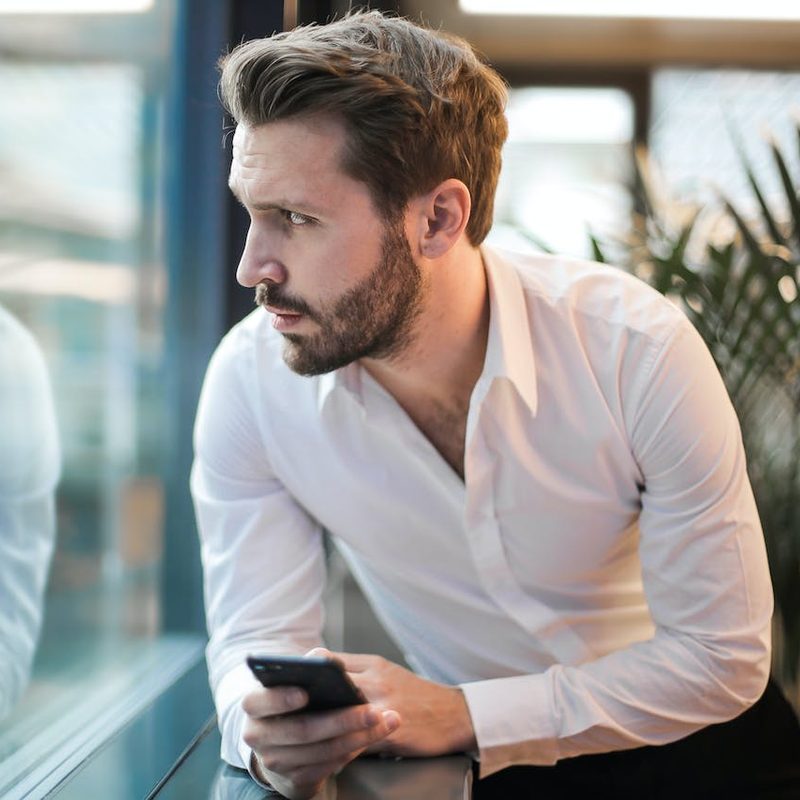 Man looking out window with phone in his hand waiting on a ride