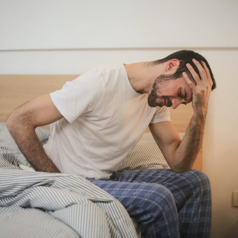 Man sitting in bed hunched over with head in hands