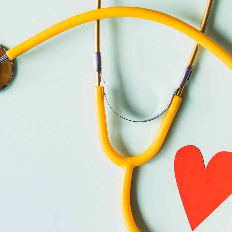 Stethoscope wrapped around a small paper red heart on a light blue background