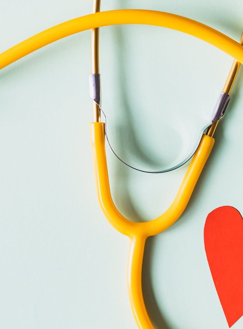 stethoscope wrapped around a small paper red heart on a light blue background