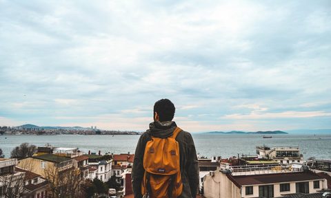 A man pictured from behind wearing a backpack and looking out over the coast in Turkey