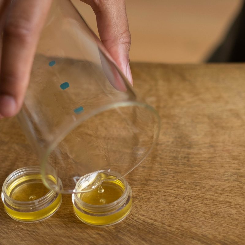 Close-up of person pouring oil into lip balm containers