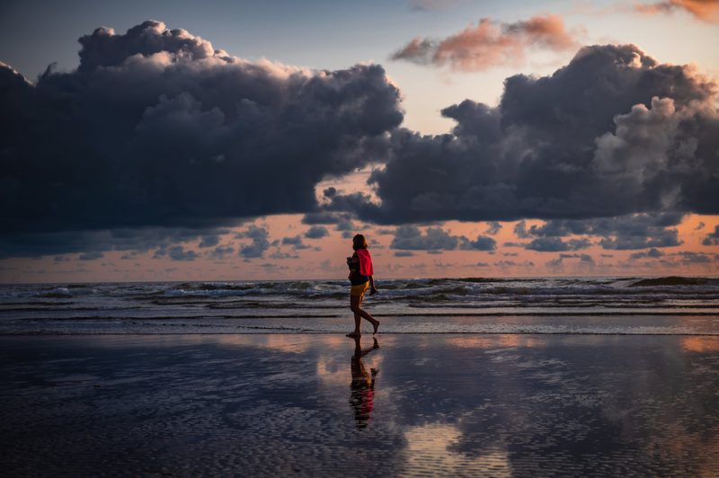 Person walking on beach with clouds in the sky