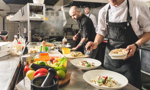 Professional chef cooking in the kitchen restaurant at the hotel, preparing dinner. A cook in an apron makes a salad of vegetables and pizza