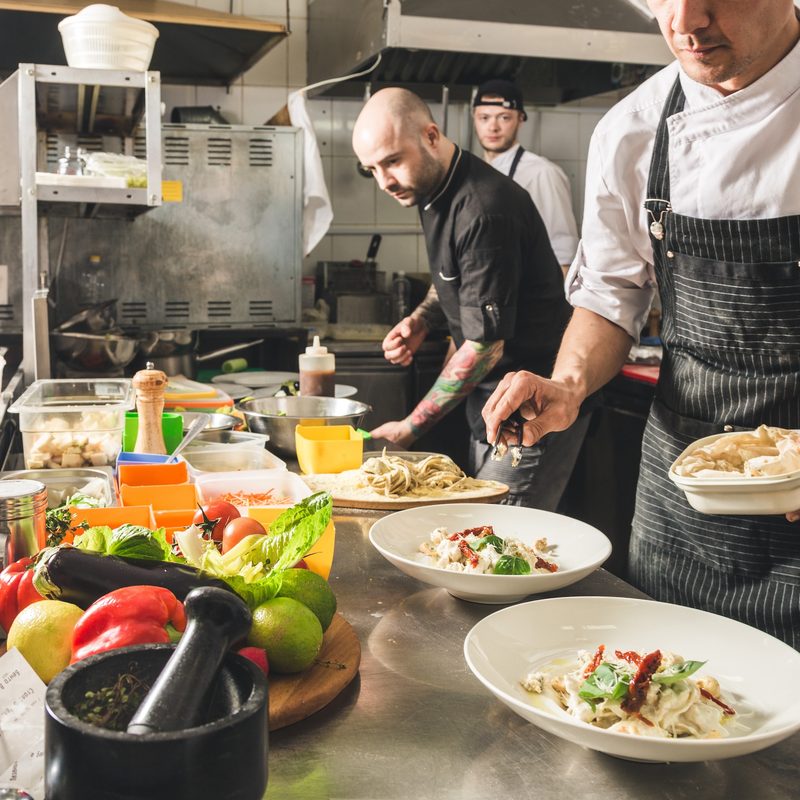 Professional chef cooking in the kitchen restaurant at the hotel, preparing dinner. A cook in an apron makes a salad of vegetables and pizza