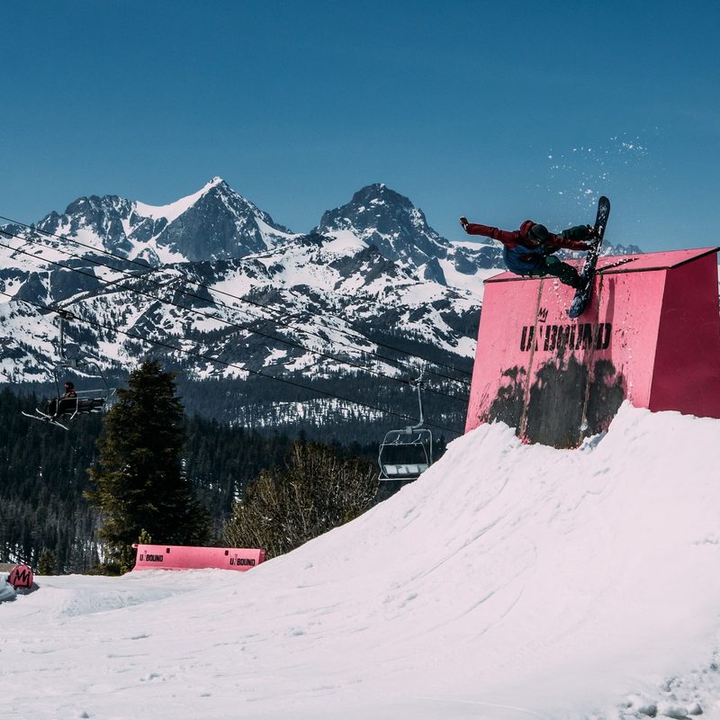 A snowboarder hits a park feature on their freestyle snowboard.