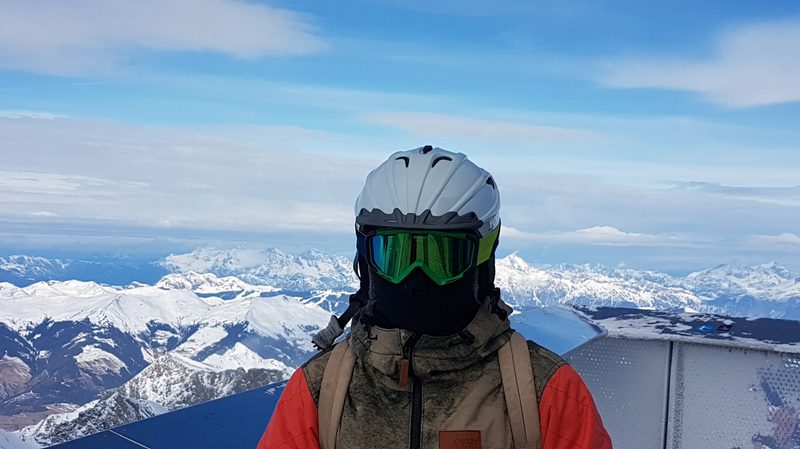 Skier with helmet, goggles, and balaclava with mountains in background