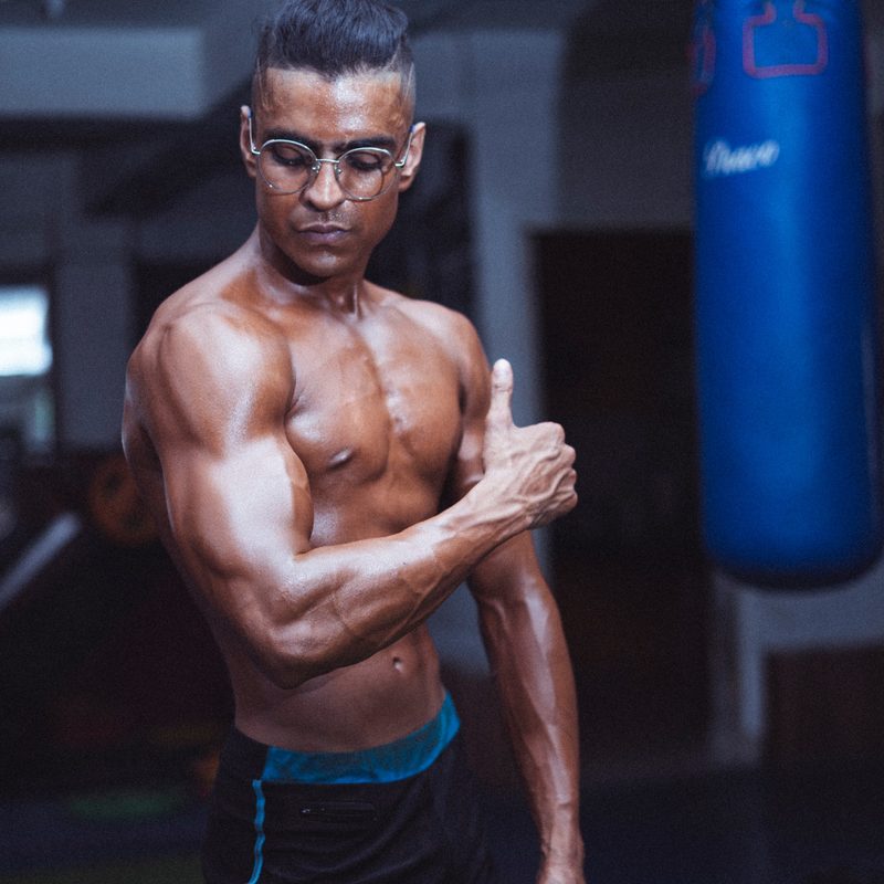 Man with no shirt flexing in gym near boxing punch bag