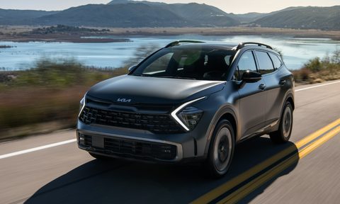 2024 Kia Sportage PHEV left front three-quarter view of a gray vehcile driving with water and mountains in the background.