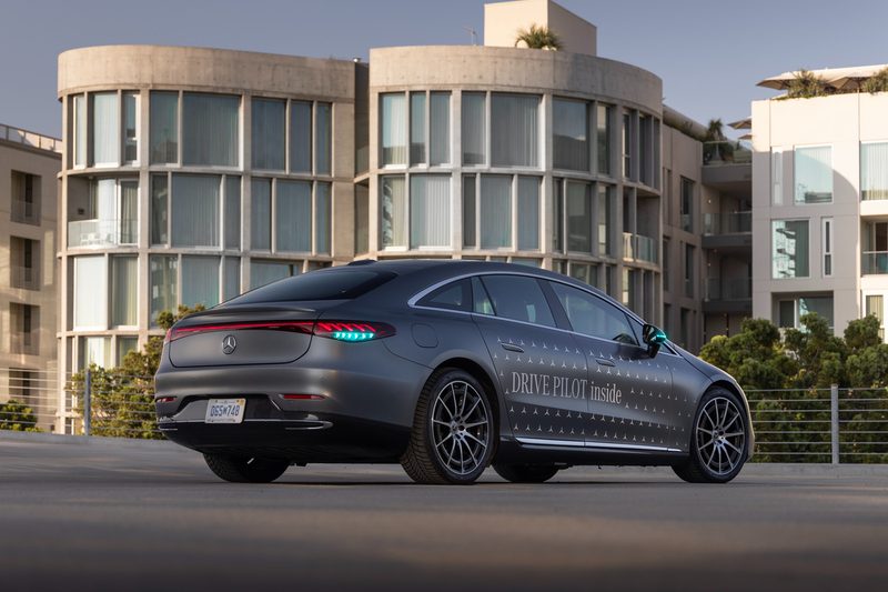 2024 Mercedes EQS equipped with Drive Pilot and turquoise lights right rear three-quarter view in front of office buildings.