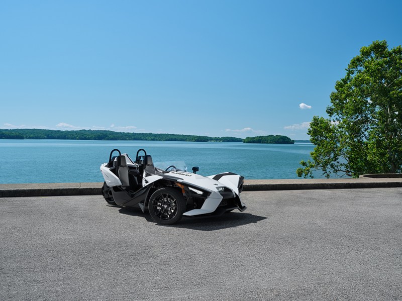2024 Polaris Slingshot S parted on pavement with a large lake in the background.