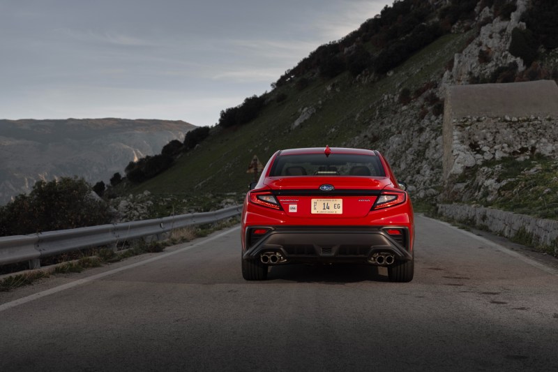 2024 Subaru WRX TR rear view of the red car driving directly away from the viewer with mountains in the background.