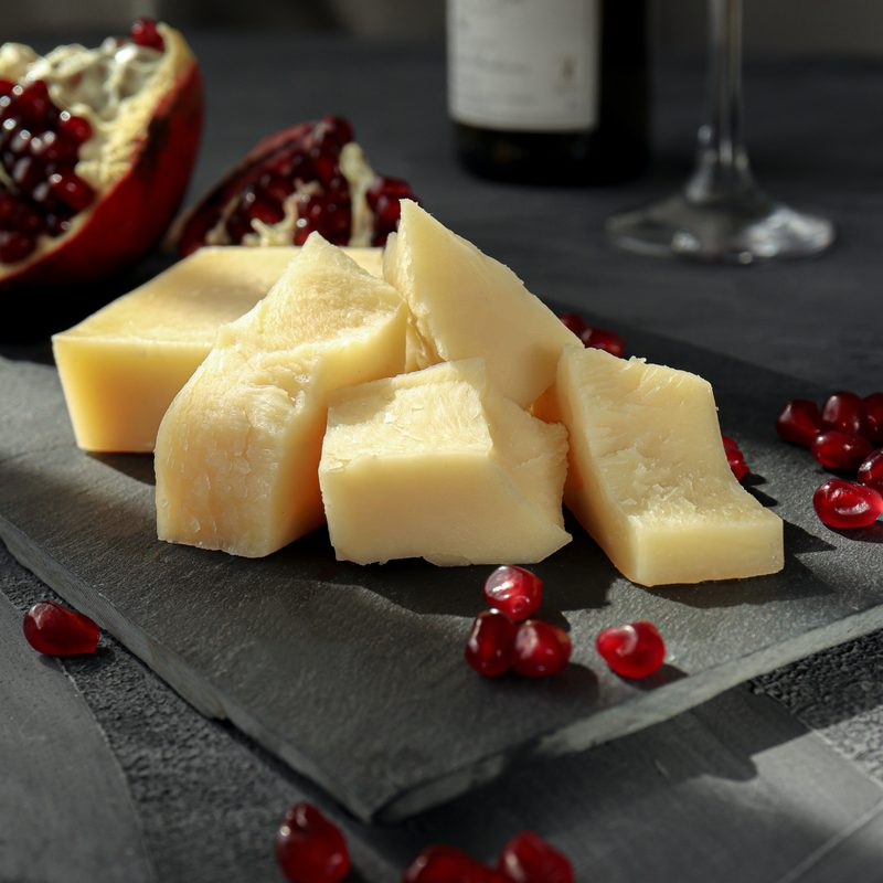 Cheese sliced on black cutting board and table with red grapes and dark background
