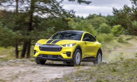 2024 ford mustang mach e rally left front three quarter view driving up a slight rise on dirt road in the woods
