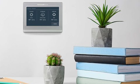 Resideo Honeywell Home smart thermostat installed on a wall with a shelf and books in the foreground.