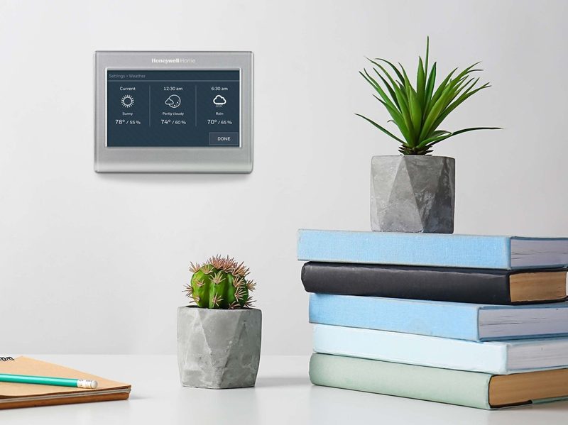 Resideo Honeywell Home smart thermostat installed on a wall with a shelf and books in the foreground.