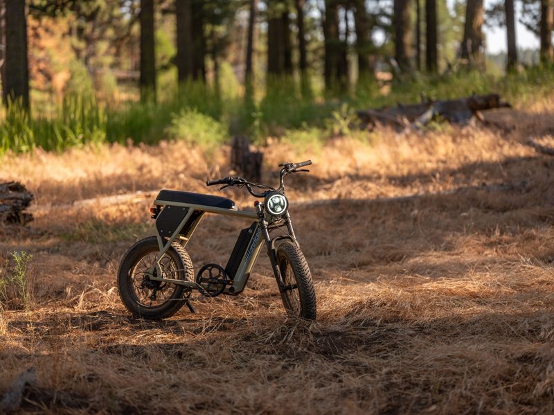 Right front three-quarter view of a Juiced Bikes Scrambler X2 parked on dried grass with a forest in the background.