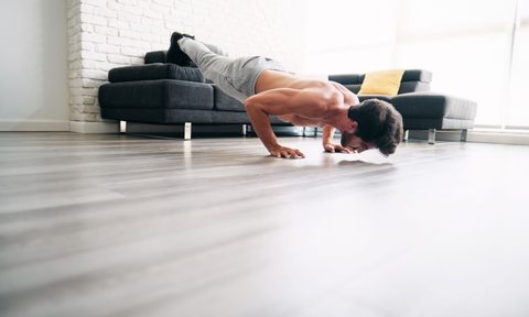Man exercising balancing plank type pose on couch at home wearing sweatpants