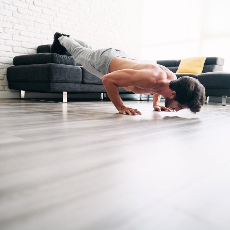 Man exercising balancing plank type pose on couch at home wearing sweatpants