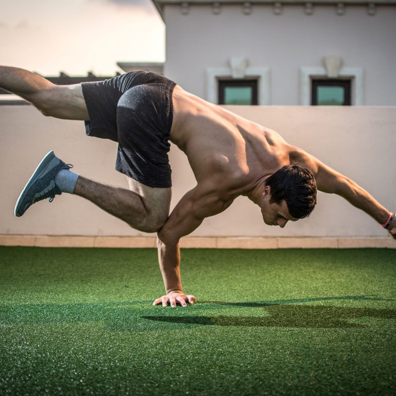 Man balancing on hand exercising on grass outside