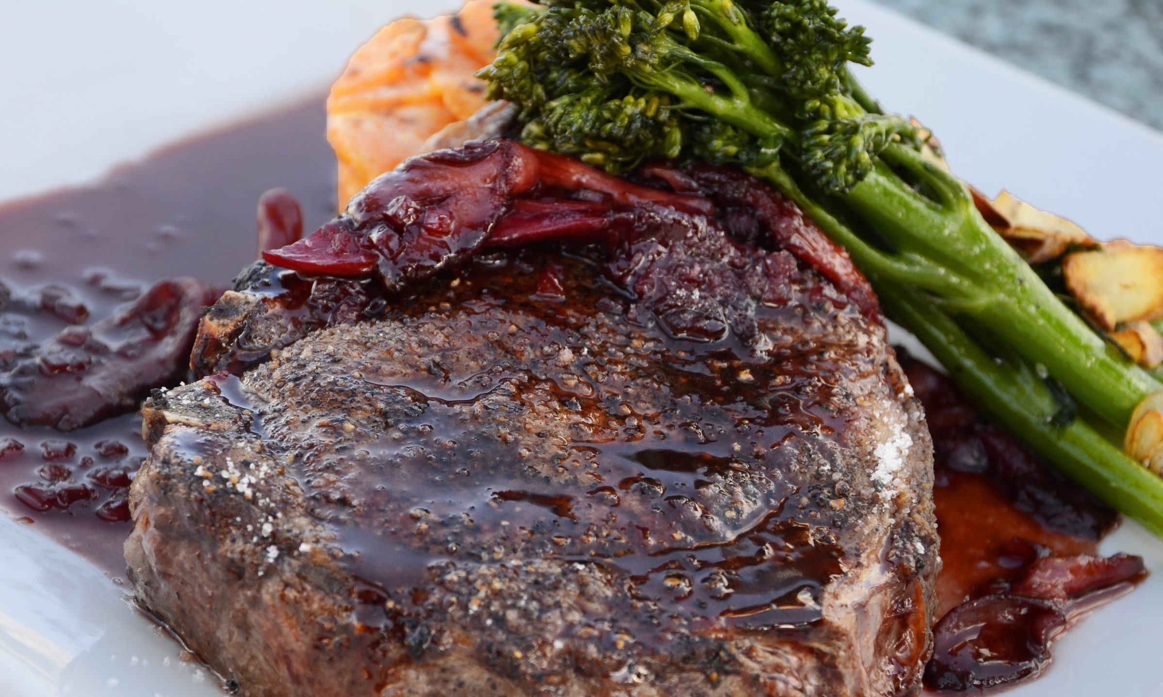 steak and broccoli on a square white plate with sauce au jus on table