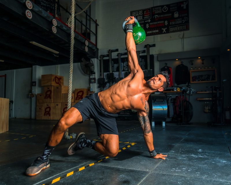 Man holding green kettleball doing pilates workout exercise gym wearing shorts no shirt