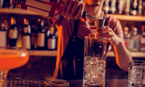 Pouring alcohol. Barman working at night and wearing uniform pouring alcohol into glass with ice