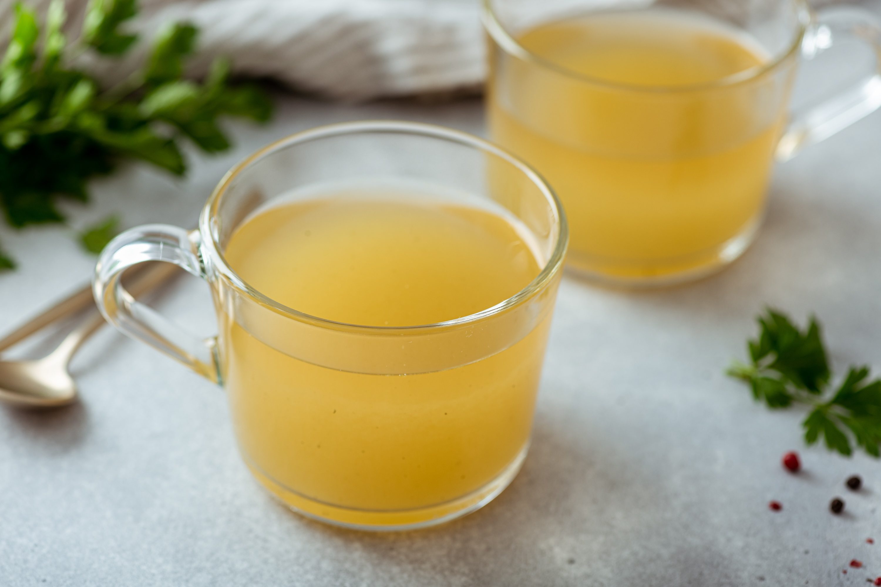 Bone broth in a glass cup on a light background, selective focus